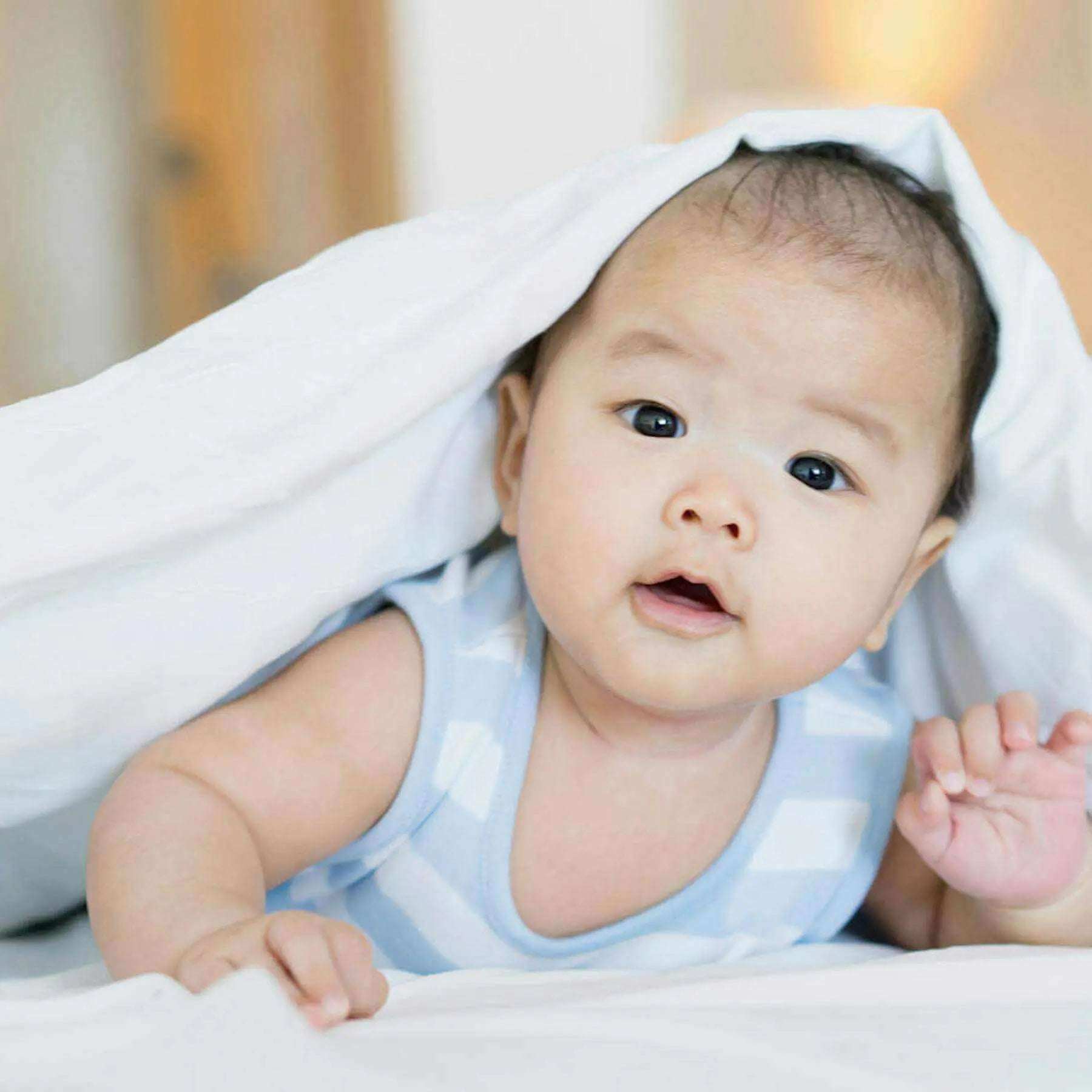 Adorable baby peeking from under white blanket, offering a charming view for new parents looking for essentials.