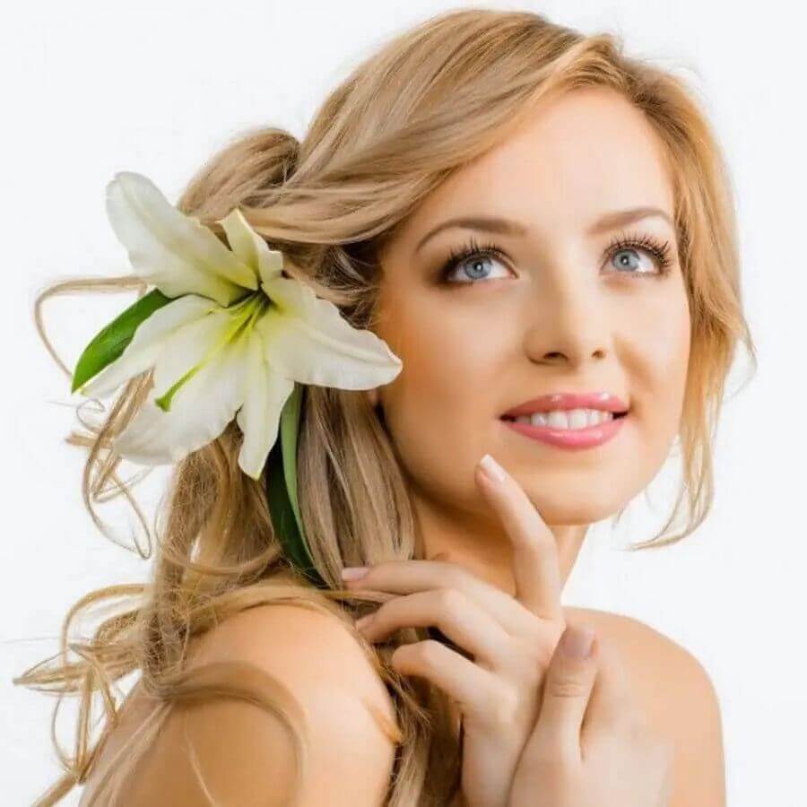 Young woman with long blonde hair and a white flower in her hair, smiling and showcasing natural beauty.