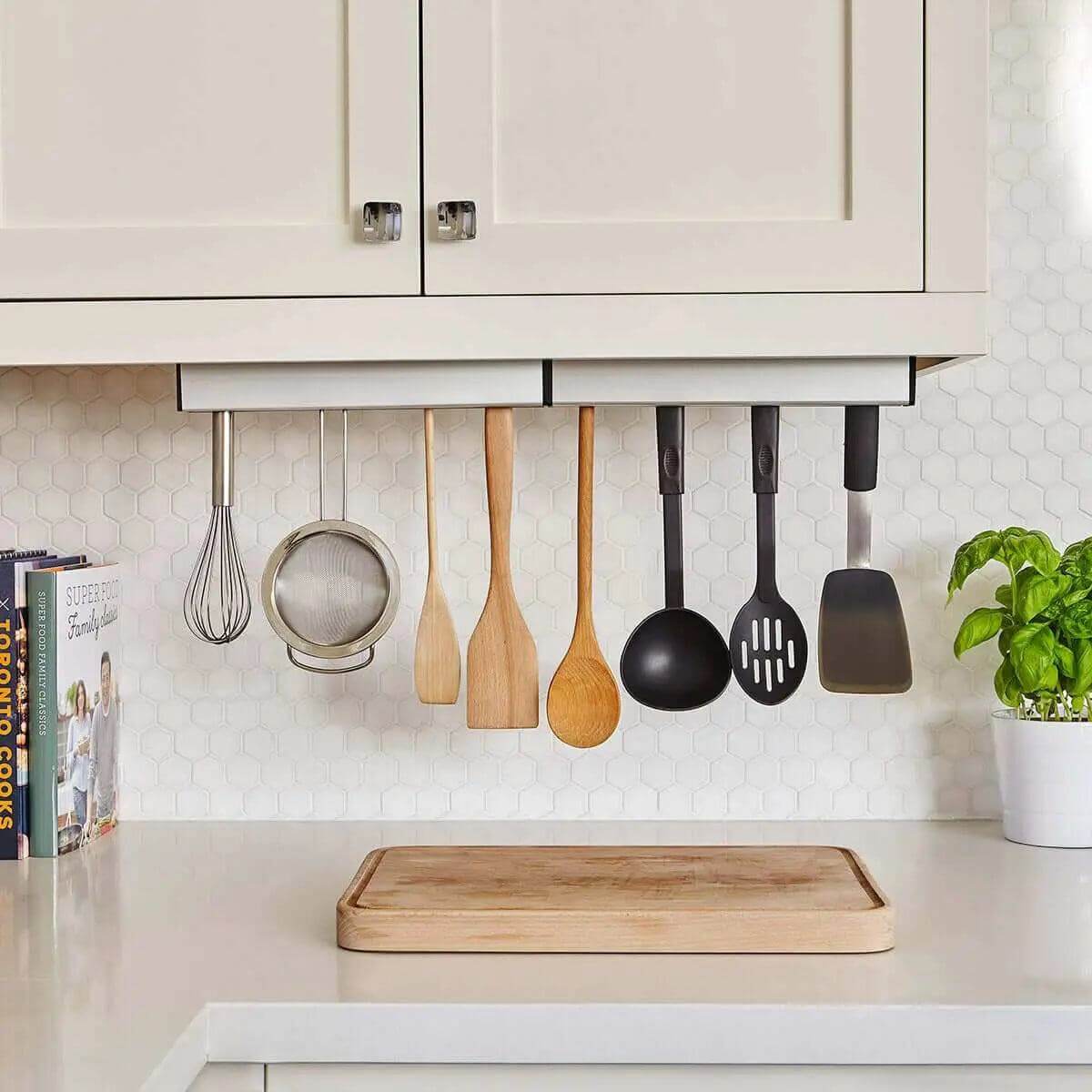 Essential kitchen accessories like spatula, whisk, and wooden spoons hanging under cabinets for meal prep efficiency.