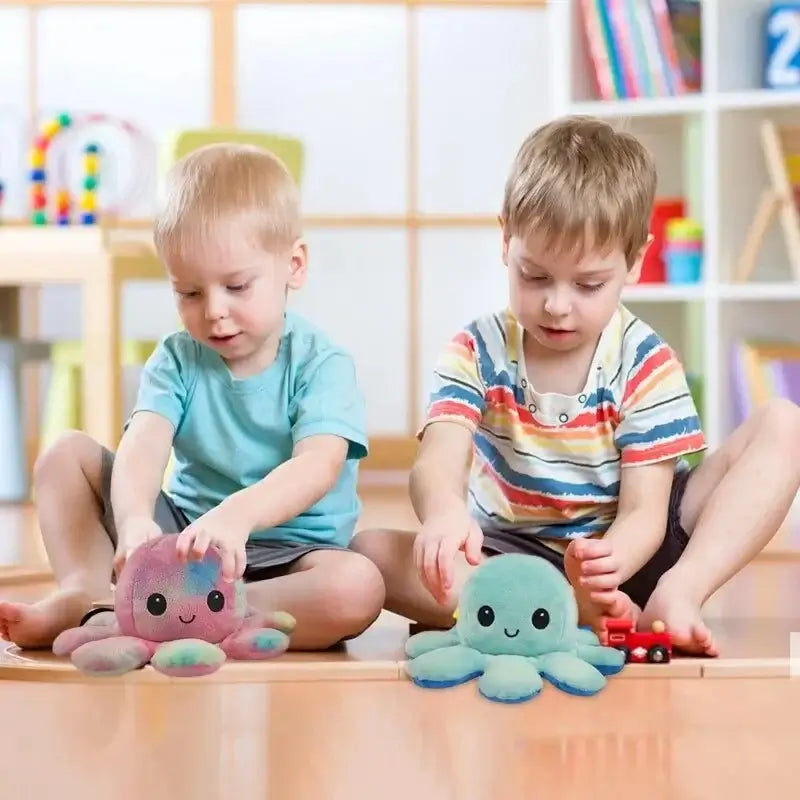 Two young boys playing with double sided flip octopus plush toys on a wooden floor in a bright, colorful room