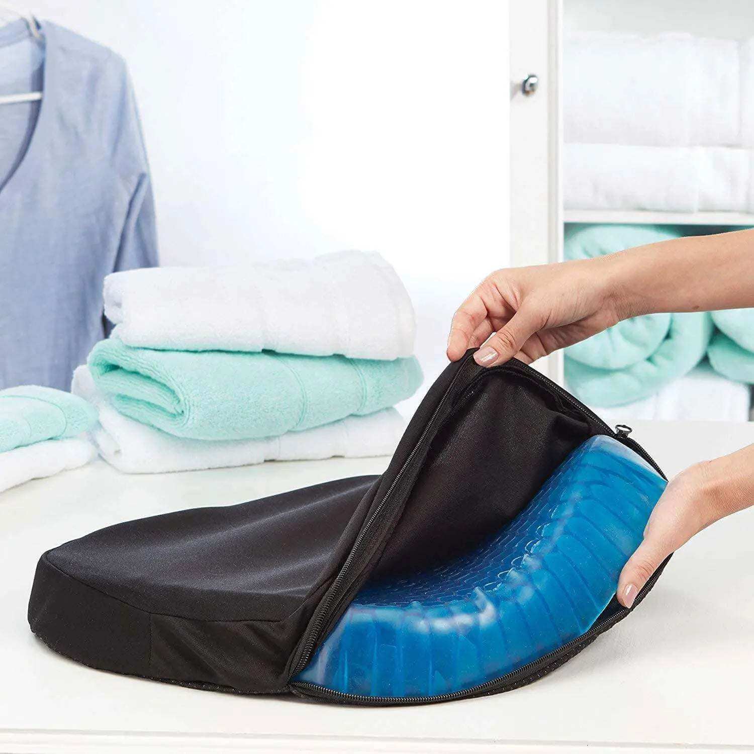 Elastic silicone egg seat cushion with blue honeycomb gel design, shown in black cover near folded towels.