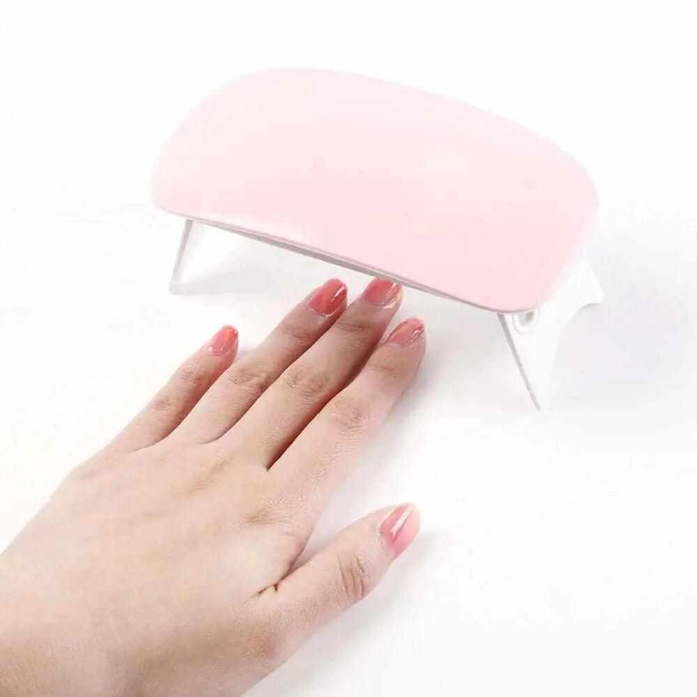 Mini portable LED UV nail dryer curing gel nail polish on hand.